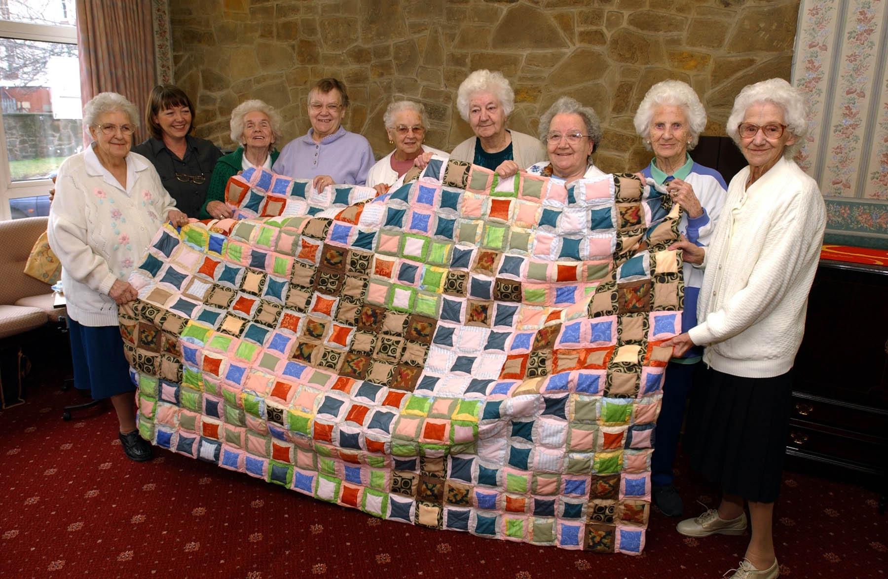 Elderly ladies holding a quilt